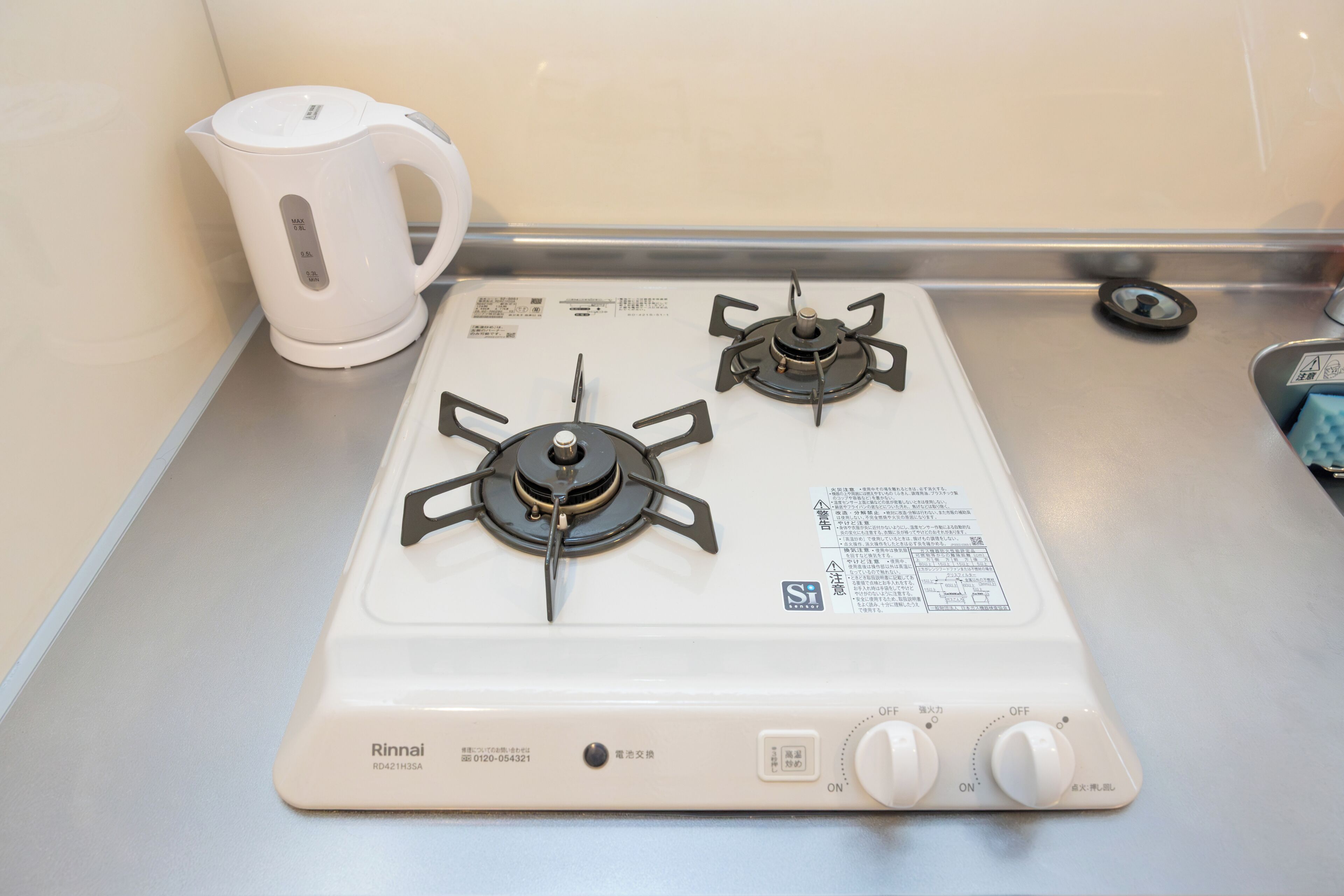 A kitchen with a white gas stove, a kettle, and a stainless steel countertop.