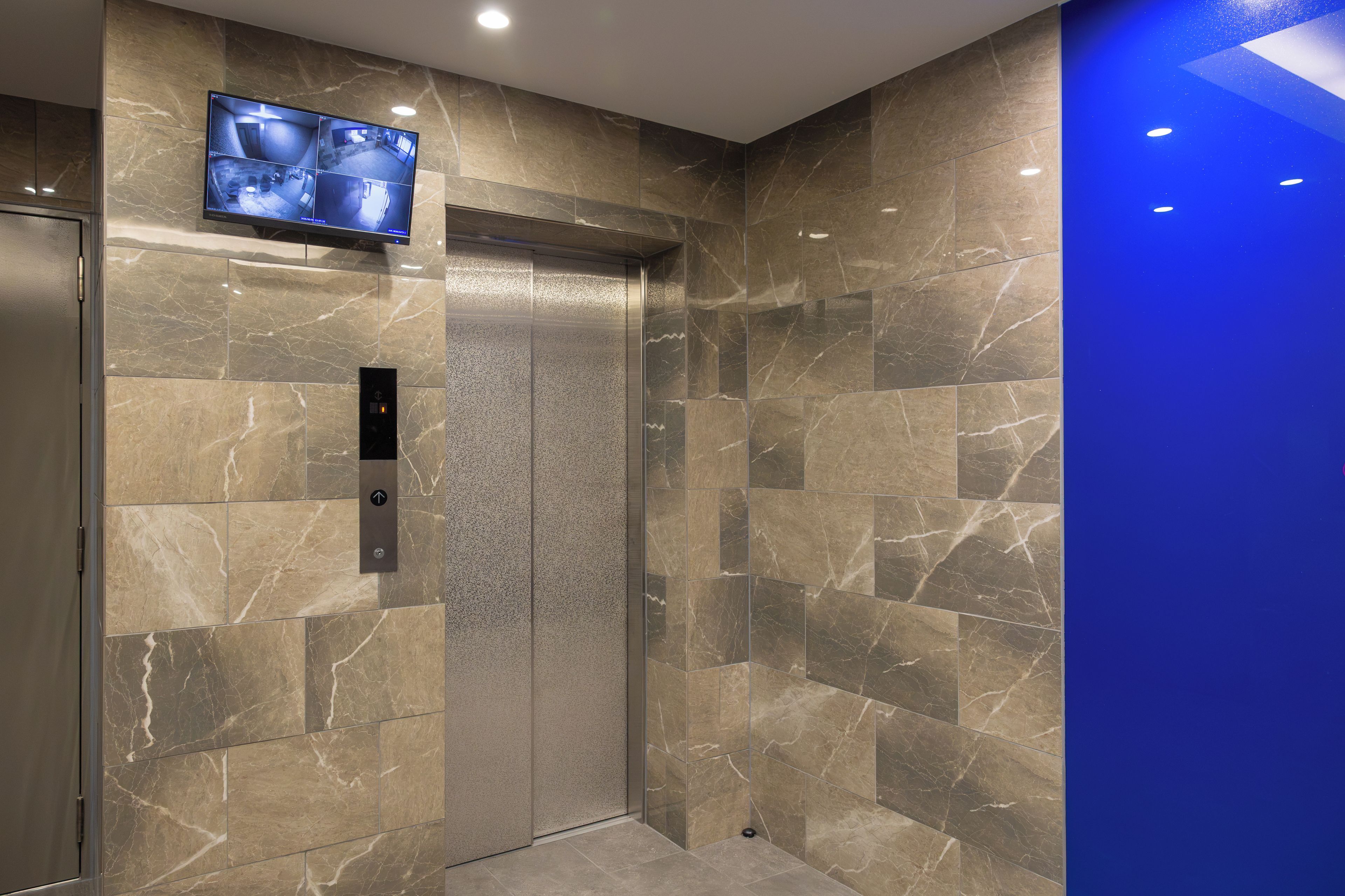 An elevator with a digital display and a control panel, surrounded by marble walls.
