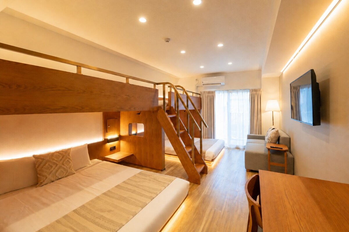 A hotel room with bunk beds, a wooden staircase, a desk, and a TV mounted on the wall.