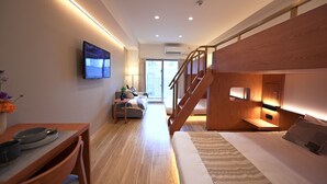 Ett modernt hotellrum med en trätrappa, en platt-TV, en soffa och en matplats med bord och stolar.