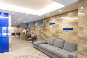 A modern lobby with a marble wall, a grey sofa, and a reception desk. - NOVI Dotonbori  (CHUO-KU OSAKA)