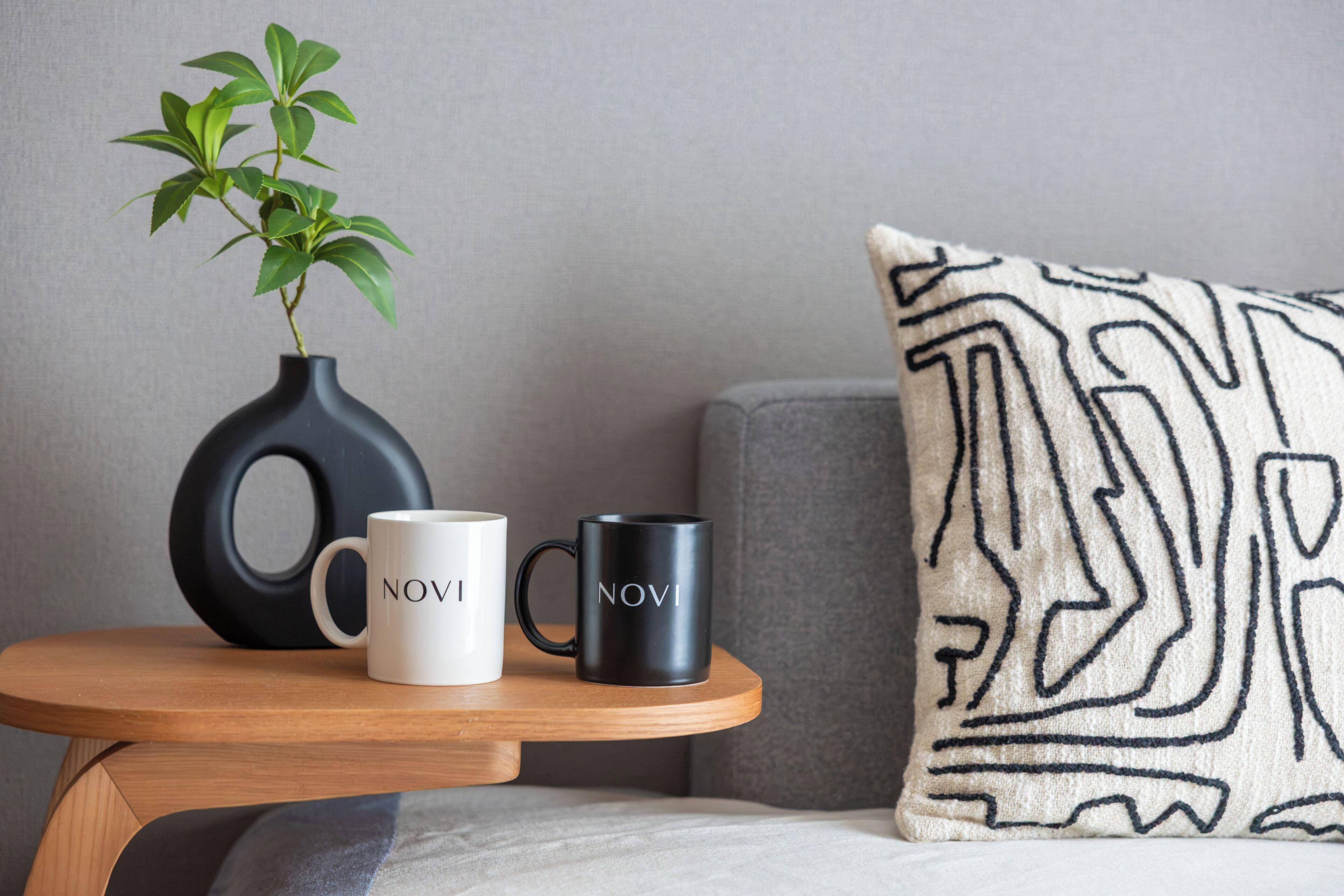 Ein kleiner Holztisch mit zwei Tassen, eine weiß und eine schwarz, und einer schwarzen Vase mit einer Pflanze darauf.