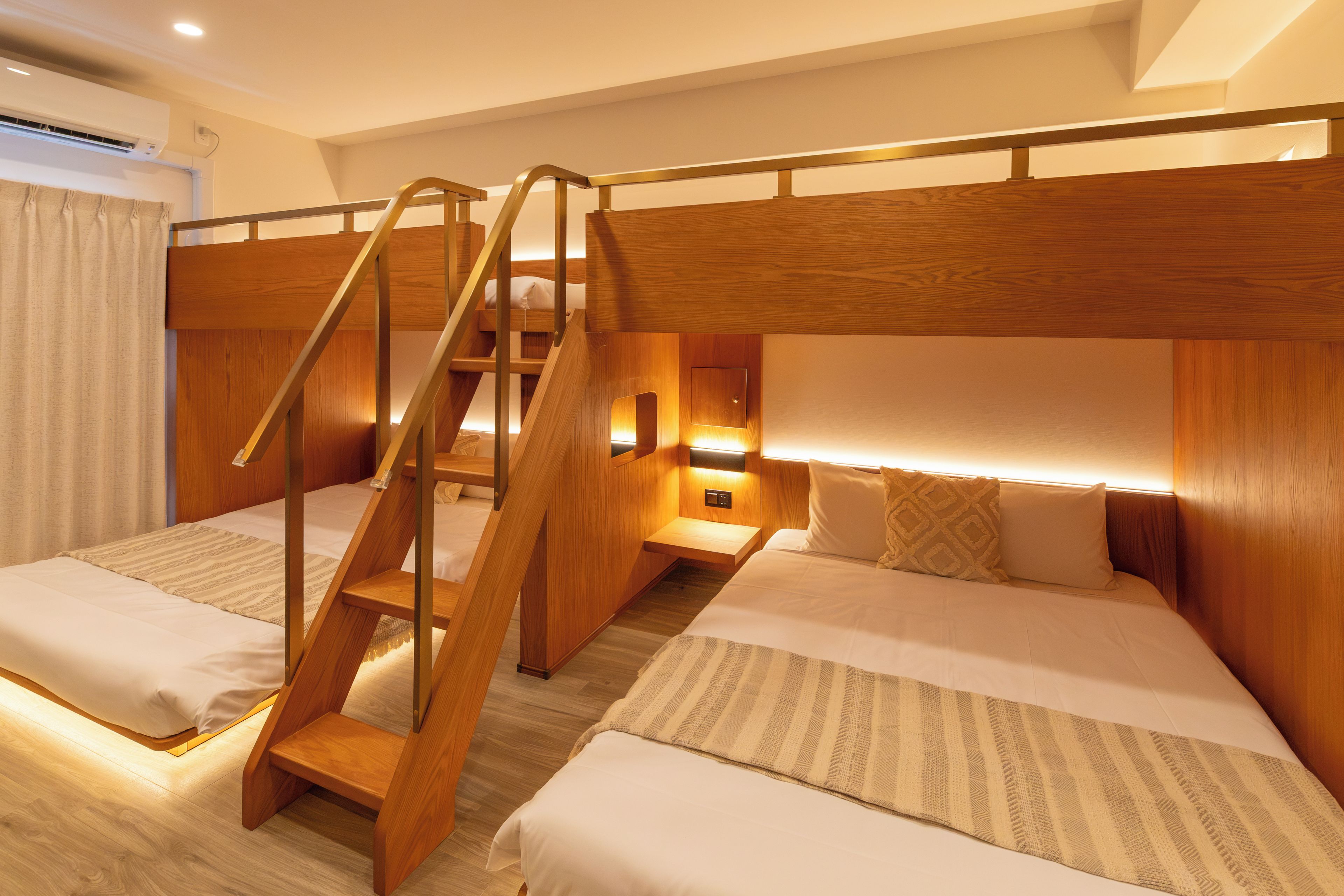 A hotel room with bunk beds, a wooden staircase, and a bedside table with a lamp.