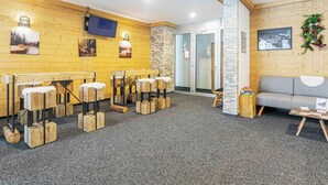 Un espace d’accueil avec des murs en bois, un canapé gris, un téléviseur fixé au mur et un escalier menant à une porte en verre.