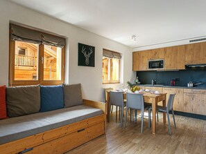 A cozy room with a wooden bench, a dining table with chairs, a kitchen with wooden cabinets, and a window with a view of a wooden structure. - T-Resort by Interhome (La Tzoumaz)