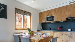 A modern kitchen with wooden cabinets, a microwave, and a dining table set for four. - T-Resort by Interhome (La Tzoumaz)