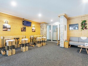 A reception area with wooden walls, a grey sofa, a TV, and a fireplace. - T-Resort by Interhome (La Tzoumaz)