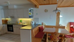 Una cucina compatta con forno a incasso, lavello e zona pranzo con una panca e sedie.