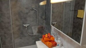 Un bagno moderno con box doccia in vetro, uno specchio grande e un portasciugamani con asciugamani piegati.