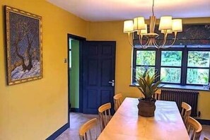Ein Esszimmer mit Tisch, Stühlen, einer Chandelierleuchtre und einer Tür sowie einem Fenster mit Blick auf Grünflächen.