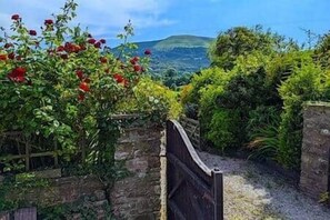 Un sentier de jardin menant à une porte d’où l’on peut admirer une colline et une végétation luxuriante.