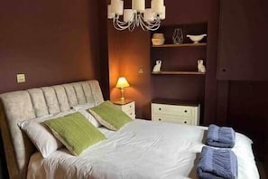 A hotel room with a bed, a nightstand, a lamp, and a shelf with decorative items.
