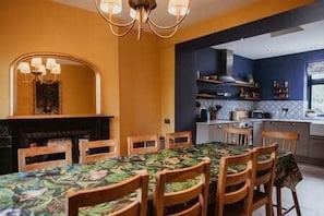A dining area with a table set for six, a fireplace, and a kitchen in the background.