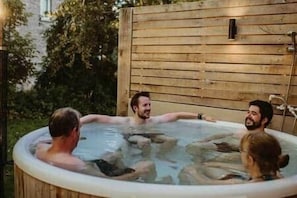 Un bain à remous où se trouvent trois personnes, entouré d’une clôture en bois et de verdure.