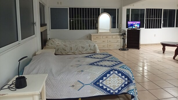 A bedroom with a bed, dresser, TV, and a fan.