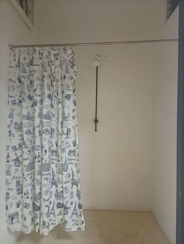 A room with a white curtain featuring Parisian landmarks and text, a simple light fixture, and a plain wall.