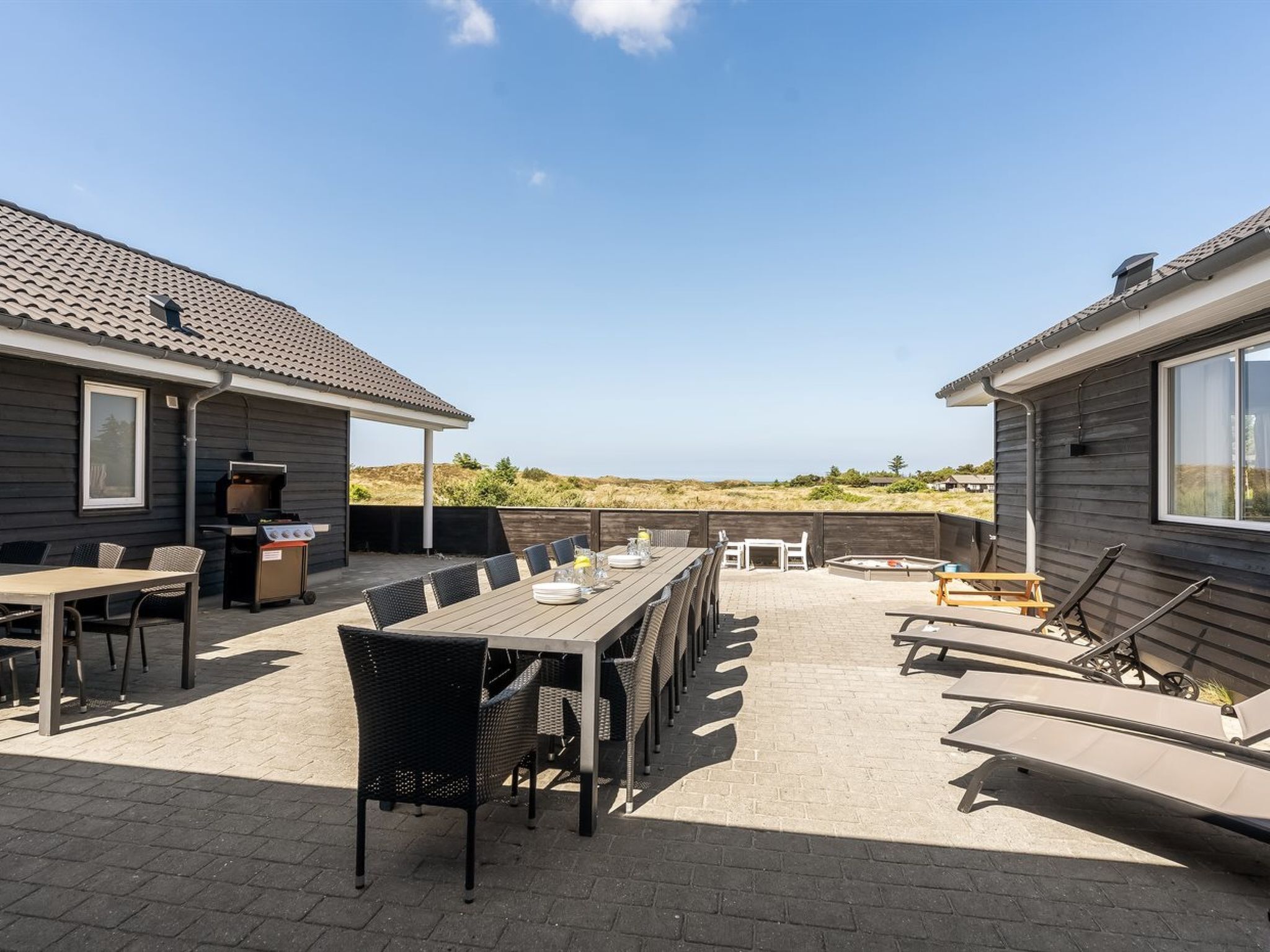 Une terrasse avec une table et des chaises, un barbecue et une vue sur les dunes.