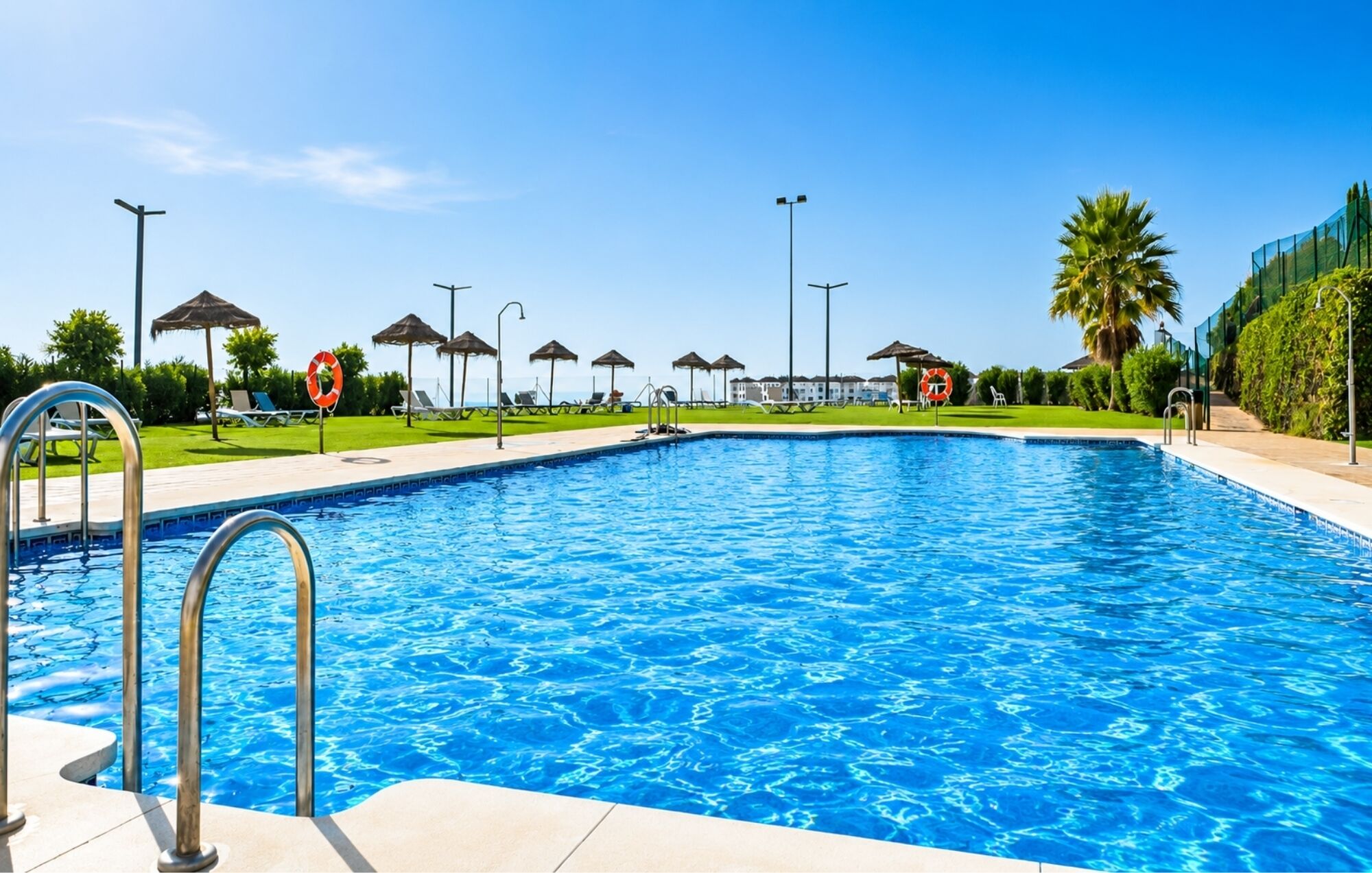 A swimming pool with a clear blue water, surrounded by lounge chairs and umbrellas, with a lifebuoy sign visible.