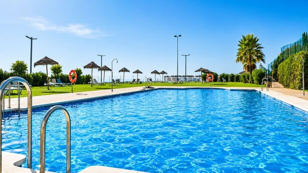 A swimming pool with a clear blue water, surrounded by lounge chairs and umbrellas, with a lifebuoy sign visible. - Elevated Hillside Apartment Close To Duquesa Marina (Manilva)