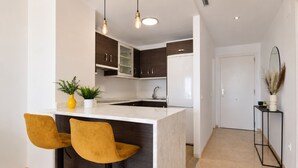 A modern kitchen with a marble island, two yellow chairs, dark wooden cabinets, and a white refrigerator. - Elevated Hillside Apartment Close To Duquesa Marina (Manilva)