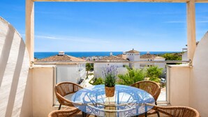 A balcony with wicker chairs and a glass table, overlooking a coastal view with buildings and the sea. - Elevated Hillside Apartment Close To Duquesa Marina (Manilva)