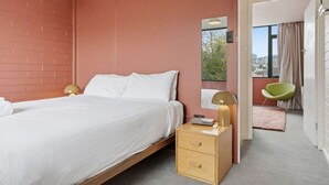 A bedroom with a bed, bedside tables, a mirror, a window, and a view of the outside.