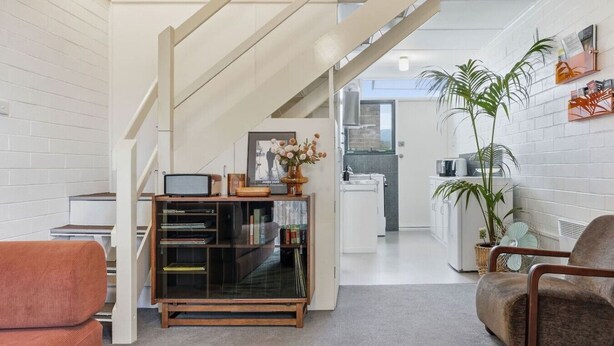 A modern living room with a staircase, a bookshelf, a coffee table, and a sofa.