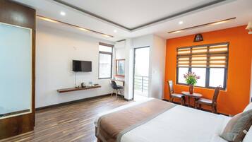 A hotel room with a large bed, a desk with a chair, a television mounted on the wall, and a window with blinds.