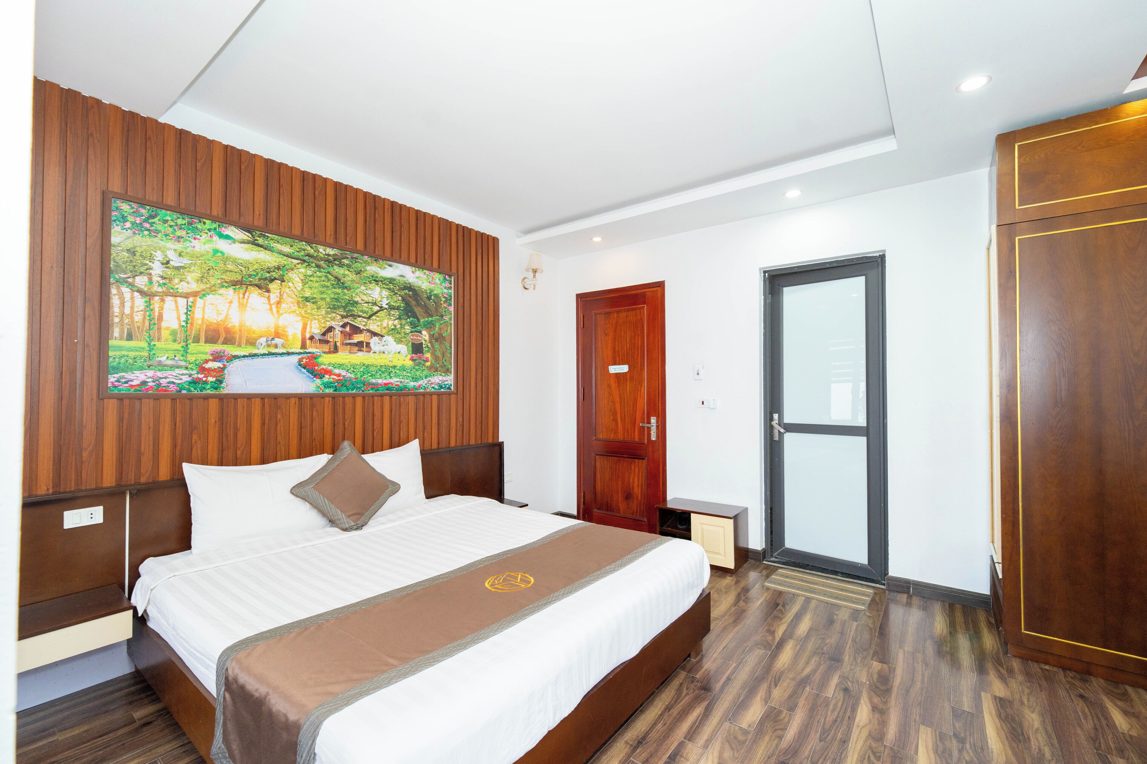 Una habitación de hotel con una cama grande, un cabecero de madera, un cuadro de un paisaje, una puerta y un armario.