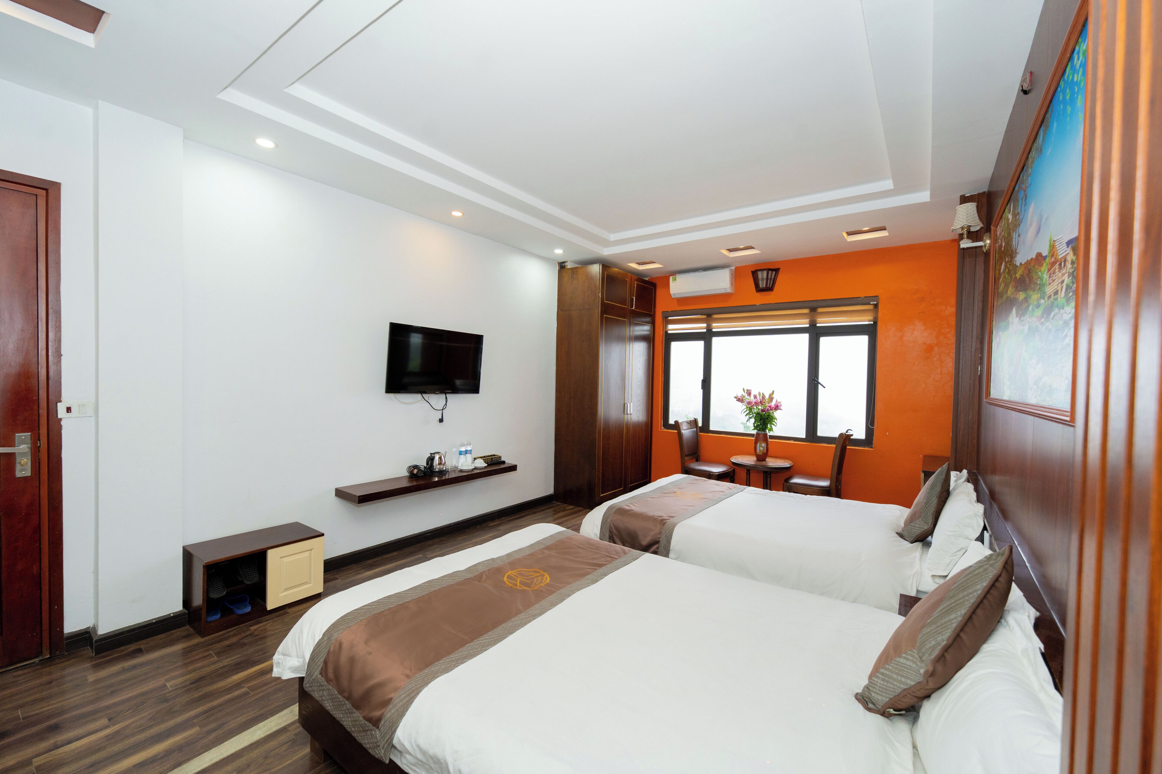 A hotel room with two beds, a TV, a window with a view, a small table with a vase, and a wooden cabinet.