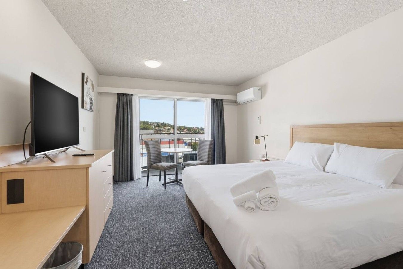 A hotel room with a bed, a desk, a television, a balcony with a table and chairs, and a view of the outside.
