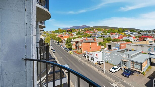 En balkon med udsigt over en gade med bygninger og et bjerg i det fjerne.