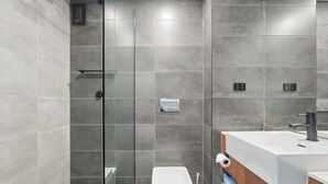 Et moderne badeværelse med bruseniche i glas, et hvidt toilet og en vask med underskab i træ.