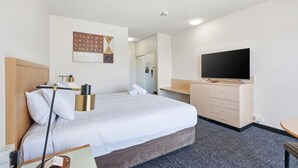 Et hotelværelse med seng, natbord, lampe, fjernsyn og et spejl.