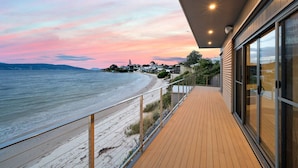 A wooden deck with a view of the beach and ocean, a glass door, and a railing. - Beachfront Escape + Hot Tub (Opossum Bay)