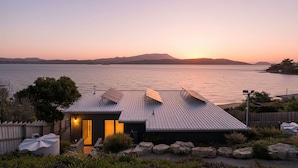 A modern house with a sloped roof, solar panels, and a view of the water at sunset. - Beachfront Escape + Hot Tub (Opossum Bay)