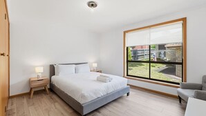 Een slaapkamer met een bed, nachtkastjes, een raam en uitzicht op buiten.