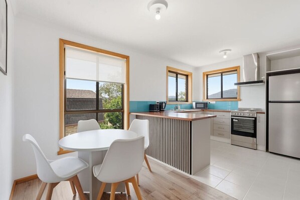 A modern kitchen with a central island, white chairs, and large windows.