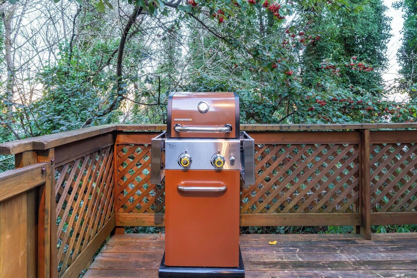 Una parrilla de barbacoa sobre una terraza de madera con un cerramiento de celosía al fondo.