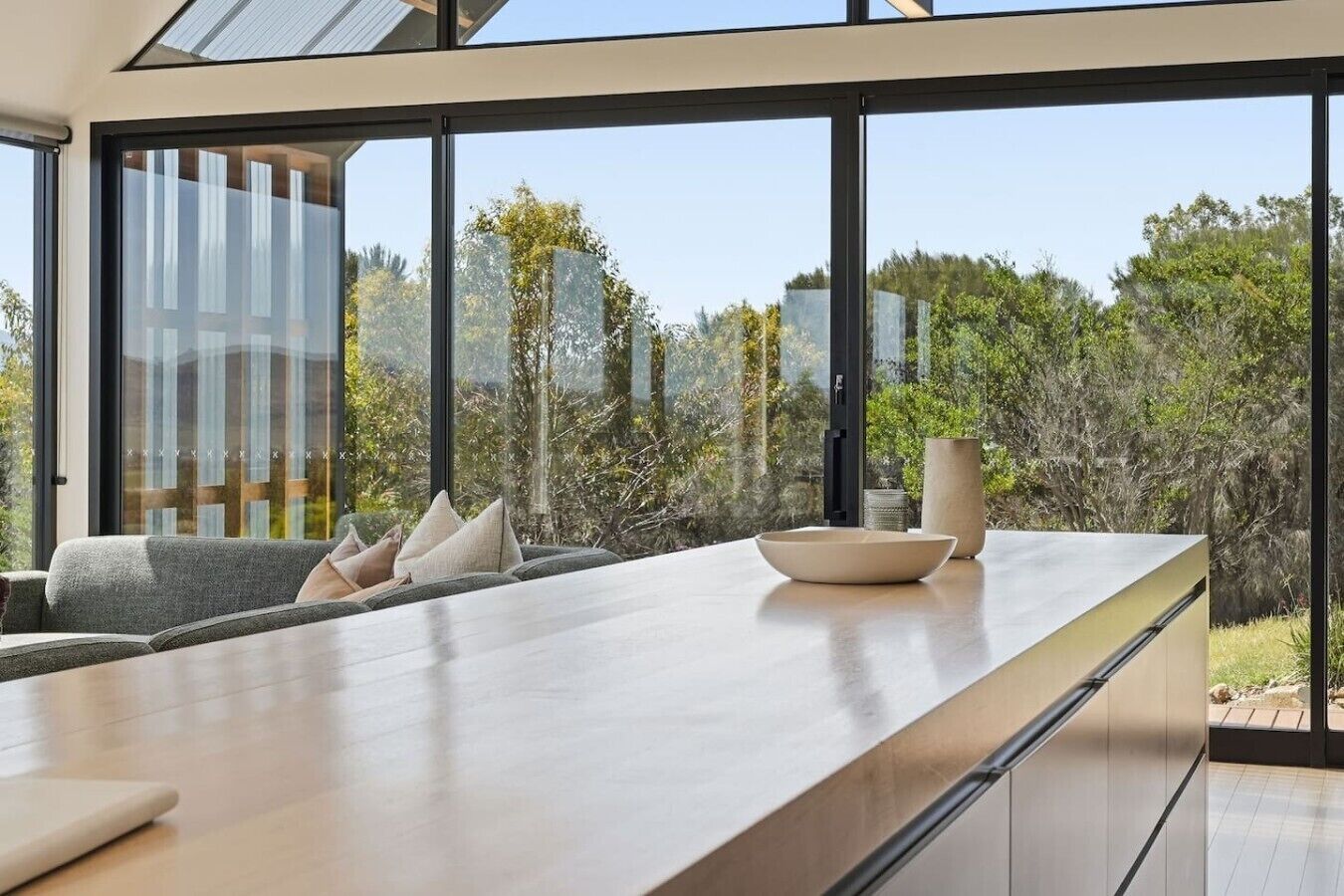 A modern kitchen with large windows, a dining area with a sofa, and a view of the outdoors.