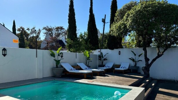 A swimming pool with lounge chairs, surrounded by a white wall and potted plants. - Blix Inn (Stellenbosch)