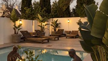 A pool area with two bronze statues, lounge chairs, and potted plants.