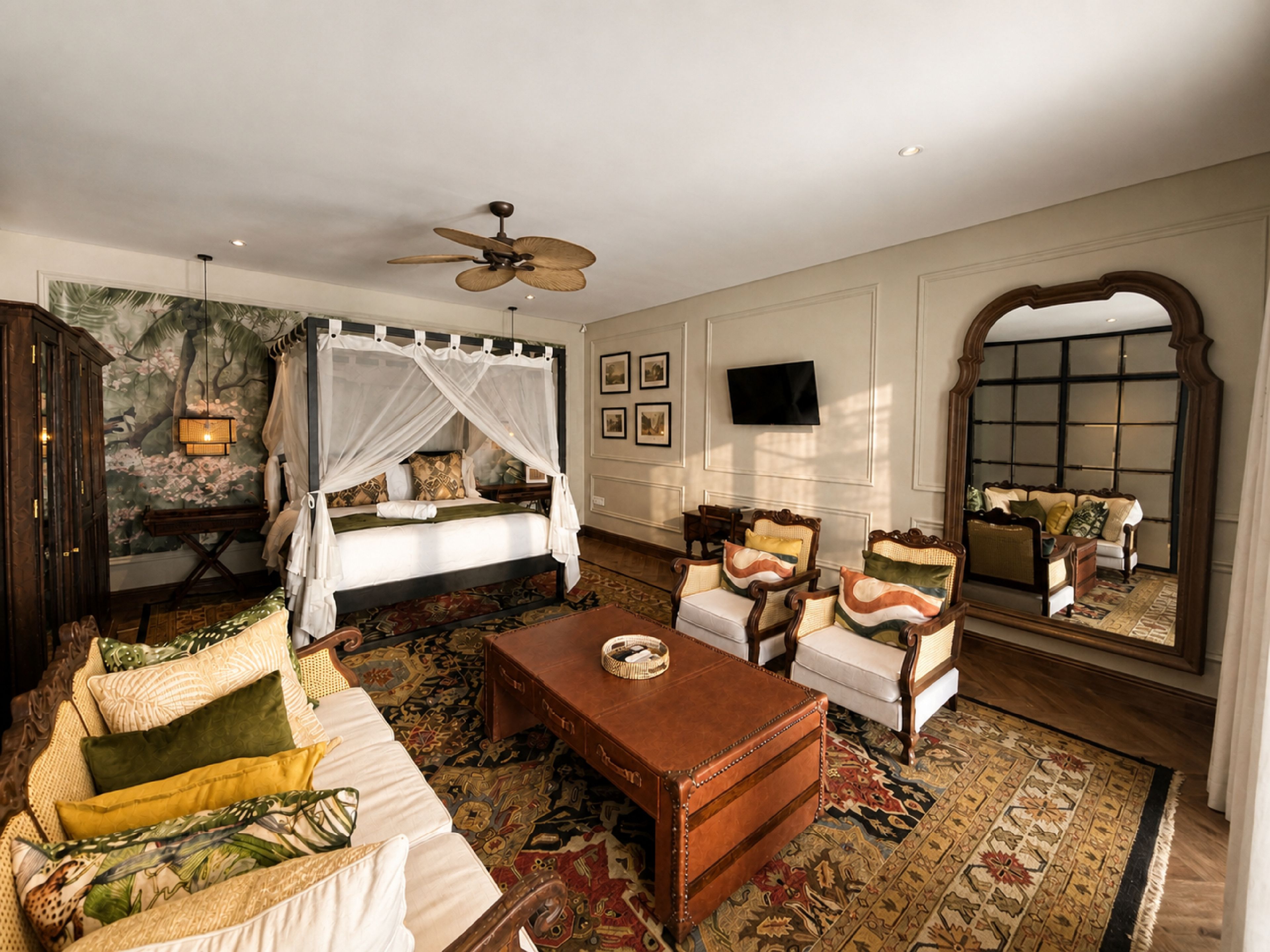 Une chambre de style traditionnel, dotée d’un lit à baldaquin, d’un ventilateur de plafond, d’un grand miroir et d’un coin salon avec des fauteuils rembourrés.