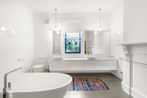A modern bathroom with a freestanding bathtub, a large mirror, and a colorful rug. - `Landport` Charming Historic Home, Modern Comforts (New Town)