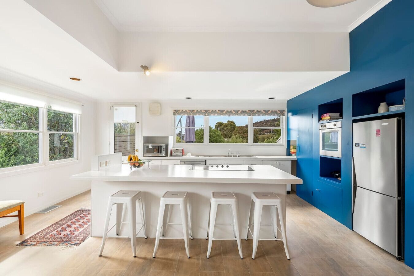 Una cocina moderna con una isla grande, taburetes de bar, un refrigerador y vistas a zonas verdes.