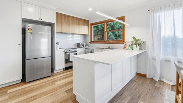 A modern kitchen with a central island, stainless steel appliances, wooden cabinets, and a large window with a view.