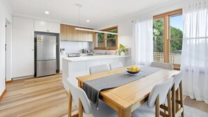 A modern kitchen with a central island, a dining area with a wooden table, and a view of greenery outside.