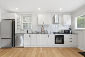 A modern kitchen with white cabinets, a stainless steel refrigerator, a dishwasher, a stove, and a microwave. - Cosy South Hobart Getaway (Dynnyrne)