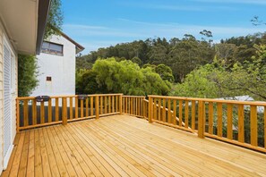 A wooden deck with a railing, a white building, and a forested hillside in the background. - Cosy South Hobart Getaway (Dynnyrne)