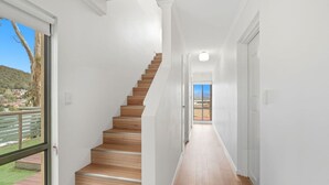 A modern interior with a wooden staircase, white walls, and a view through a large window. - Riverview Townhouse Retreat (Lindisfarne)